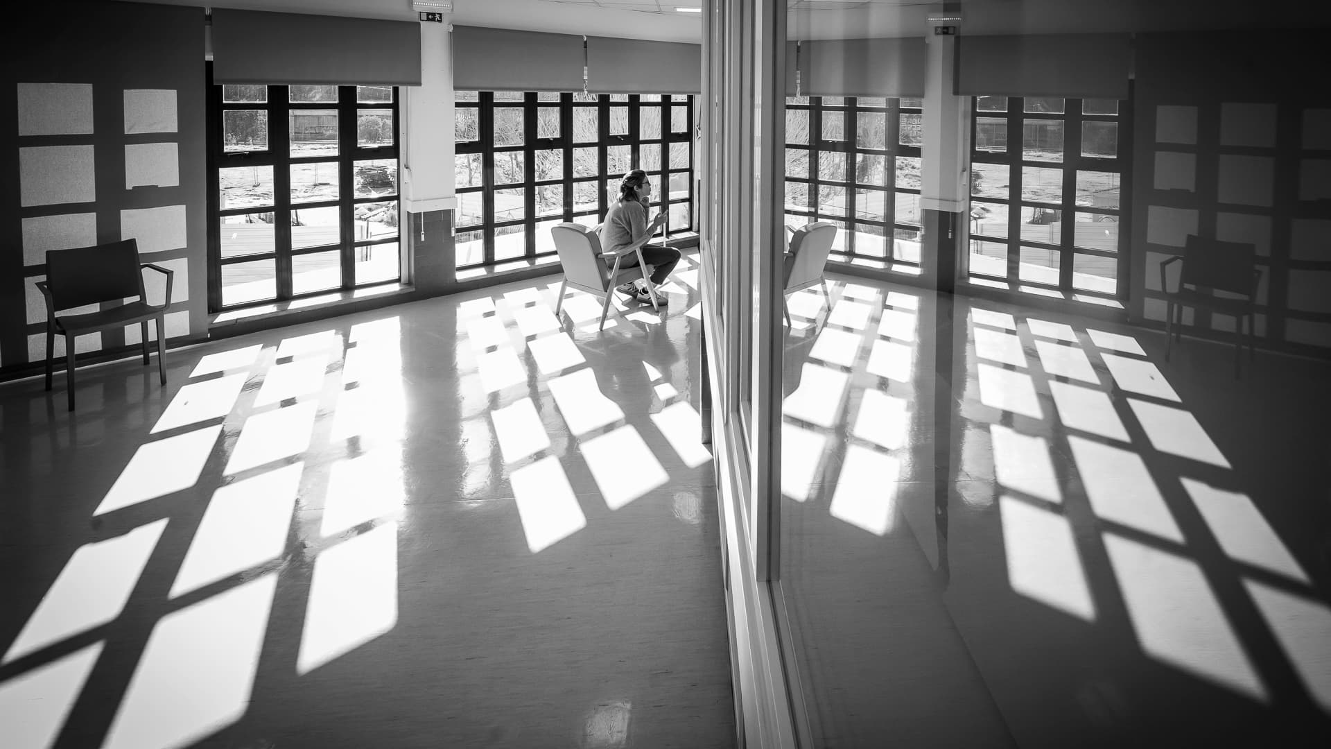 Foto a preto e branco de alguém sentado numa sala com muitas janelas