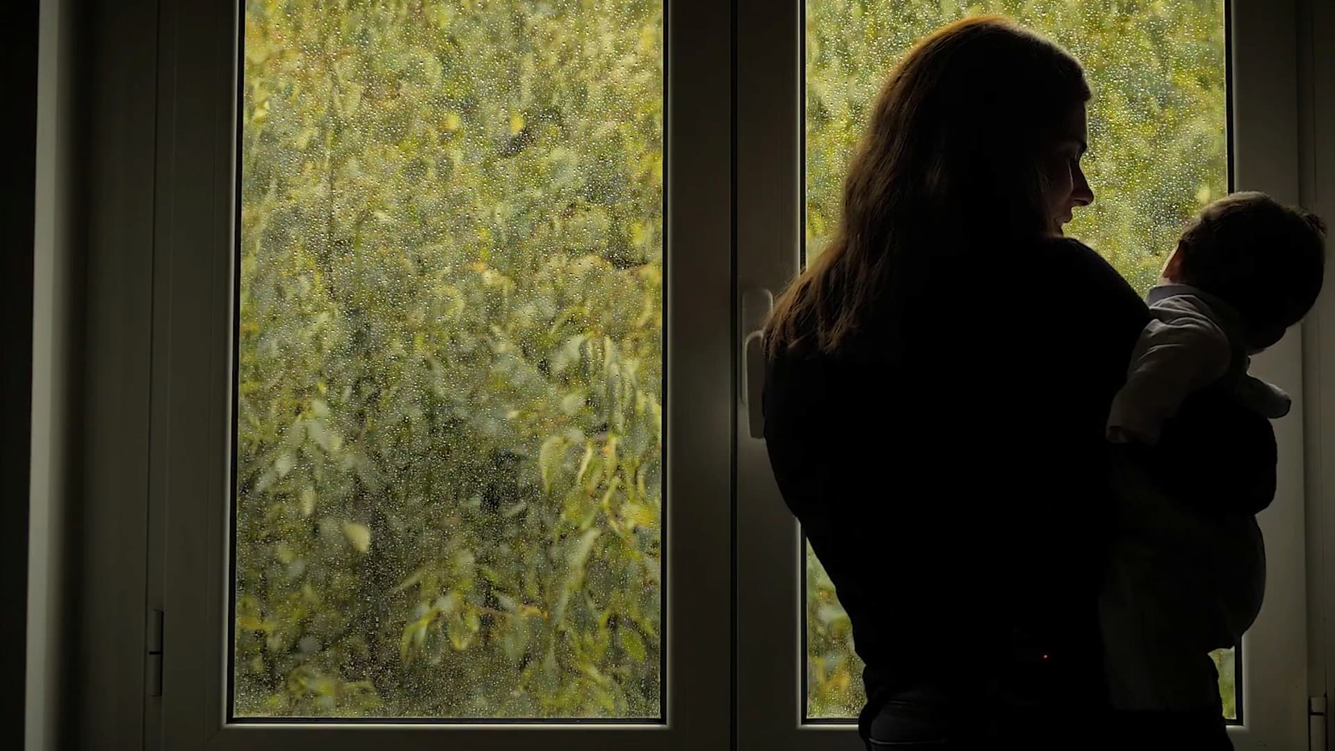 Mãe de Família de Acolhimento com bebé ao colo à janela