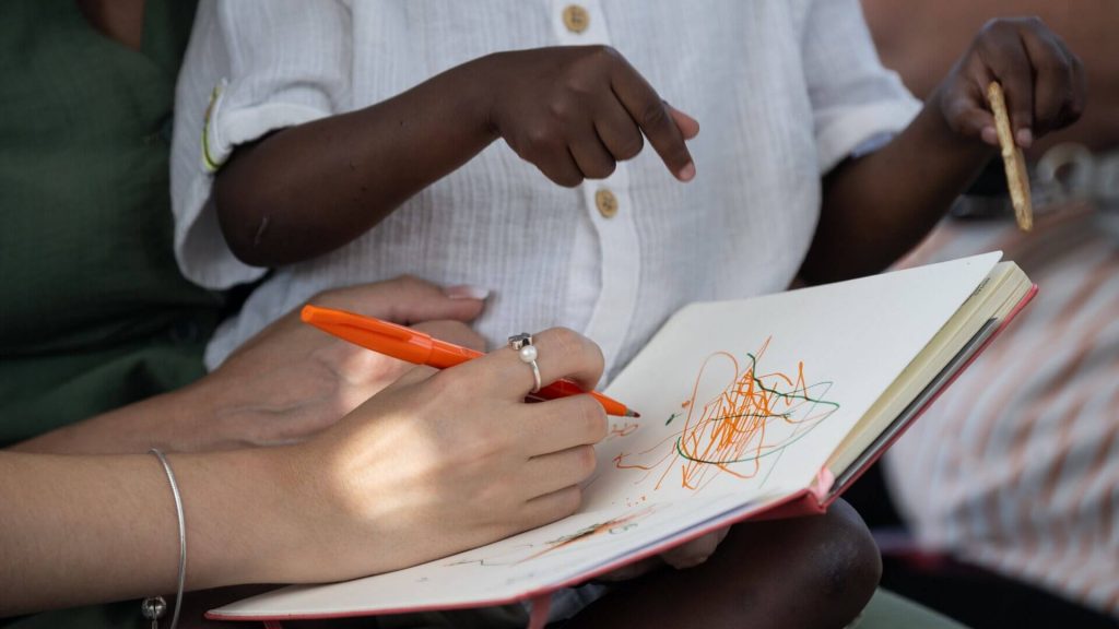 Mãos de senhora e de criança num caderno com desenhos
