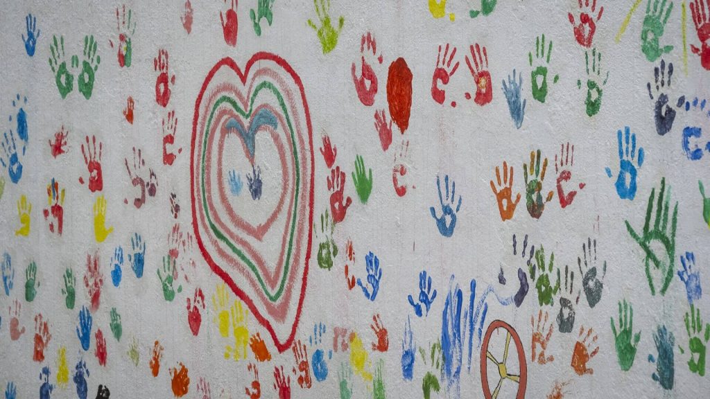 Um coração e várias palmas das mãos às cores pintados na parede
