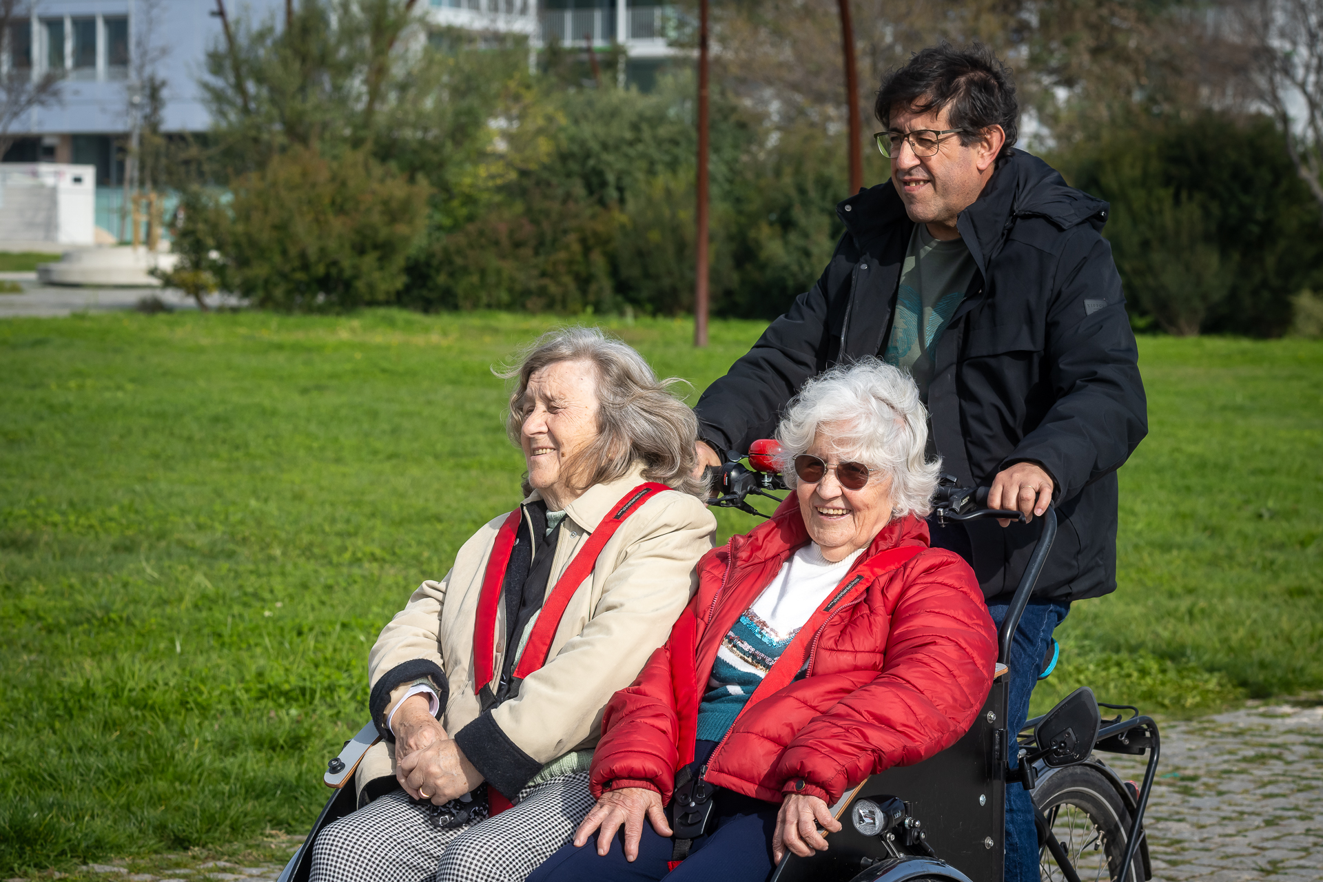 duas senhoras sentadas numa bicicleta adaptada são conduzidas por um senhor