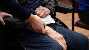 Alguém dá a mão a utente em cadeira de rodas