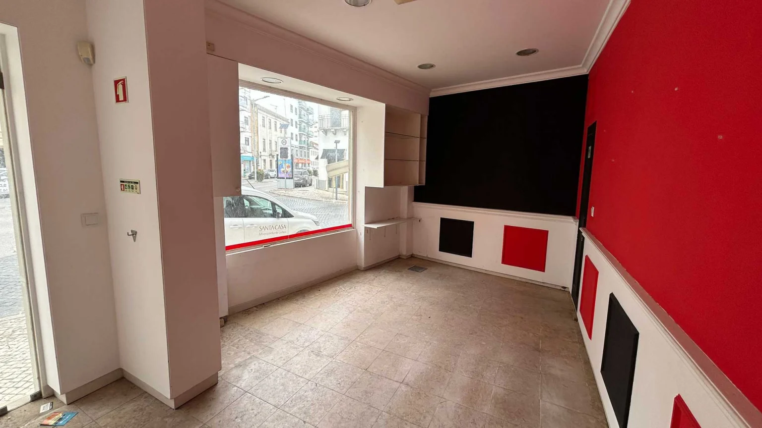 Shop interior with red walls, black panels and a shop window onto the street, at Av. Tenente Valadim, 2