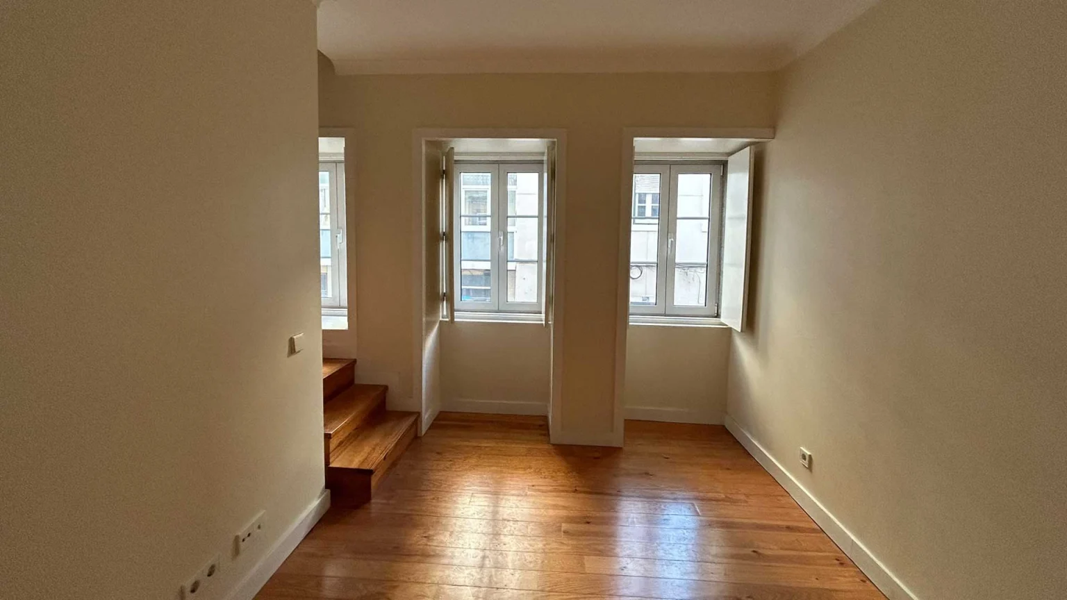 Sala com soalho de madeira, dois degraus à esquerda e duas janelas ao fundo, na Rua Silva Carvalho, 26