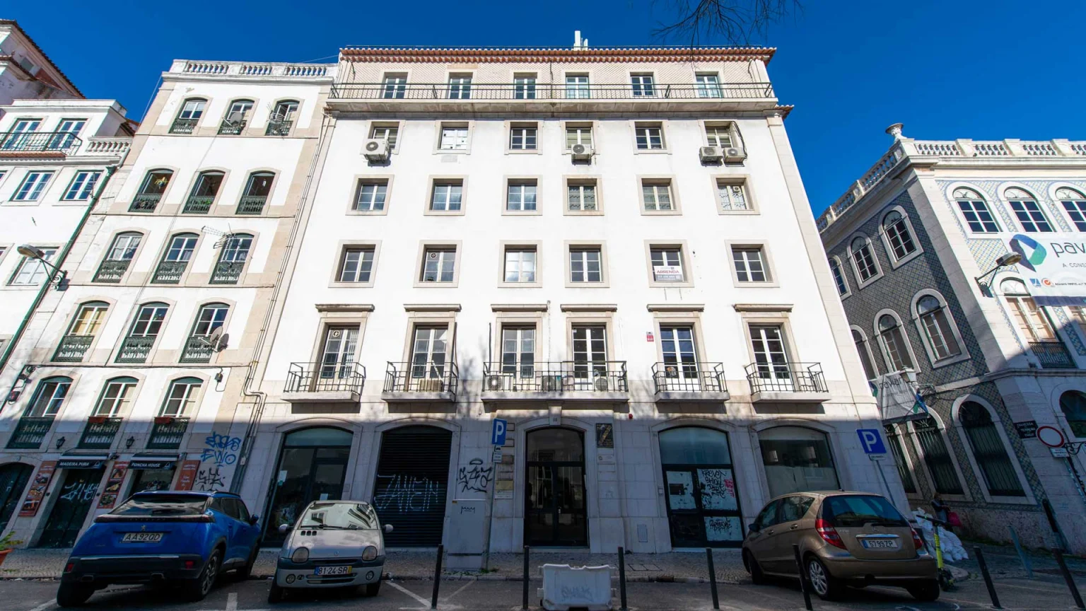 Fachada branca da Rua Terreiro do Trigo, 66 vista de frente, com carros estacionados junto à entrada
