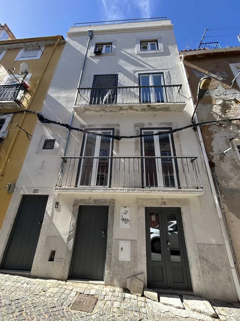 Fachada branca e estreita de quatro pisos da Travessa das Flores, 18-20, com varandas e portas verdes