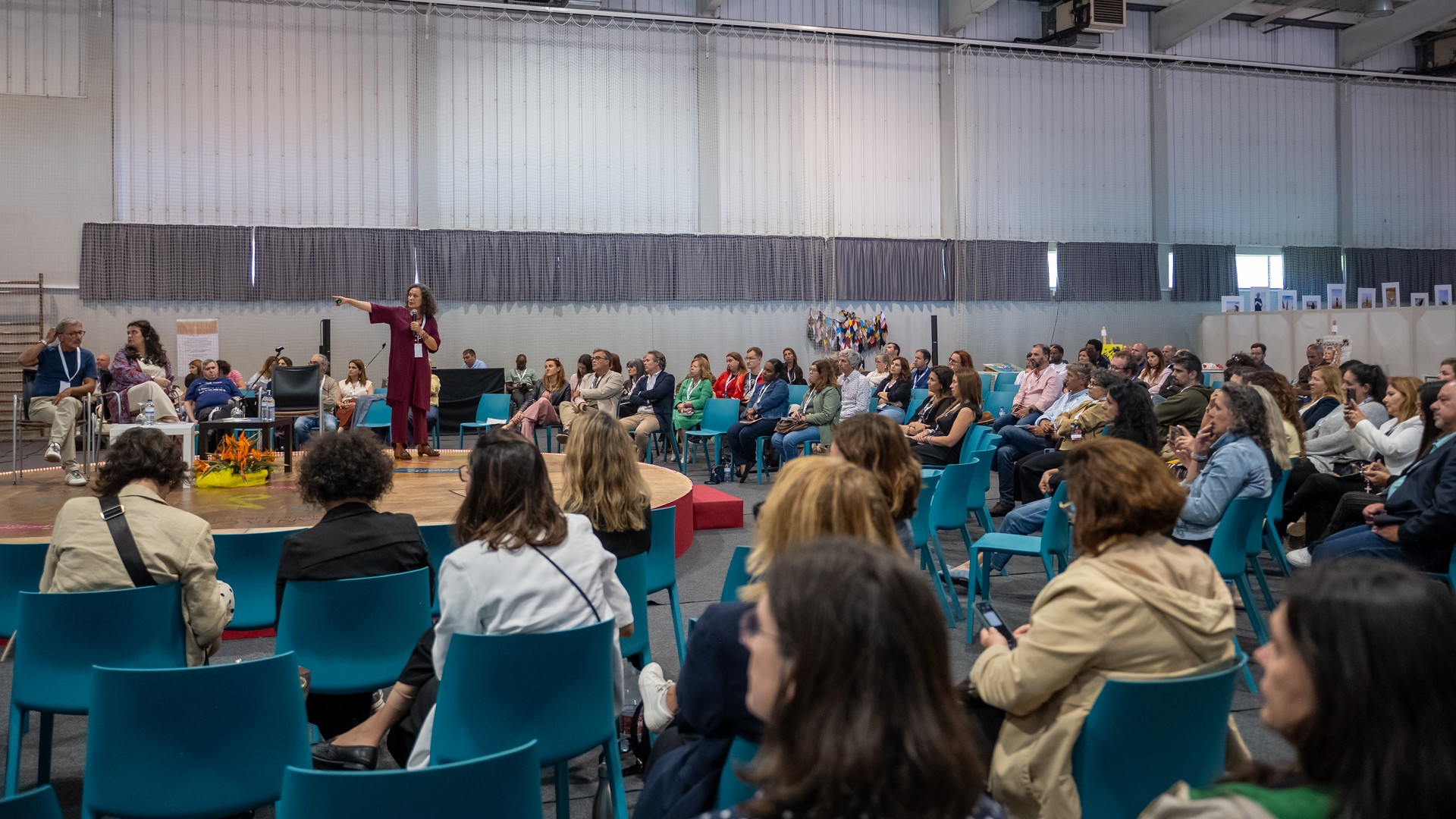 Palco com oradora, rodeada de cadeiras com participantes no seminário