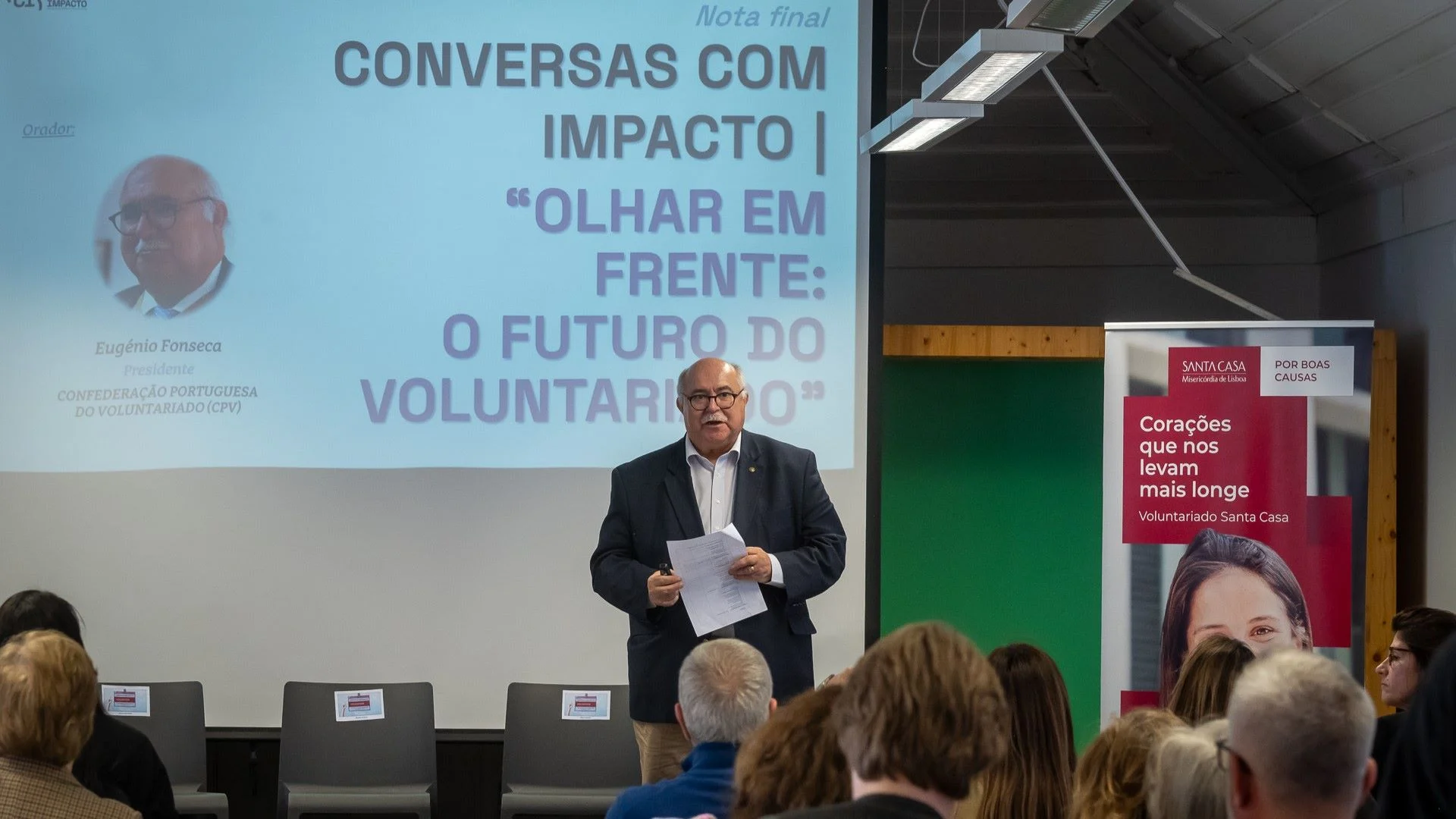 homem de pé conversa com plateia sobre voluntariado