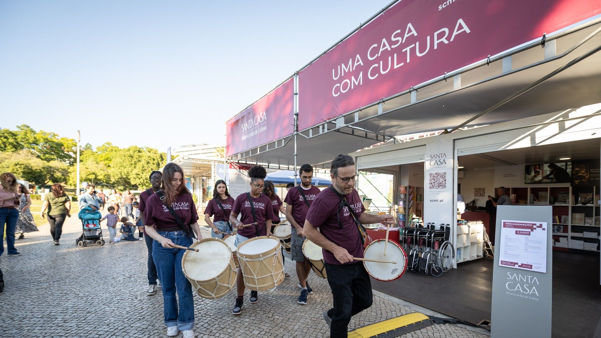 rapazes e raparigas tocam tambor em frente ao stand da scml na feira do livro