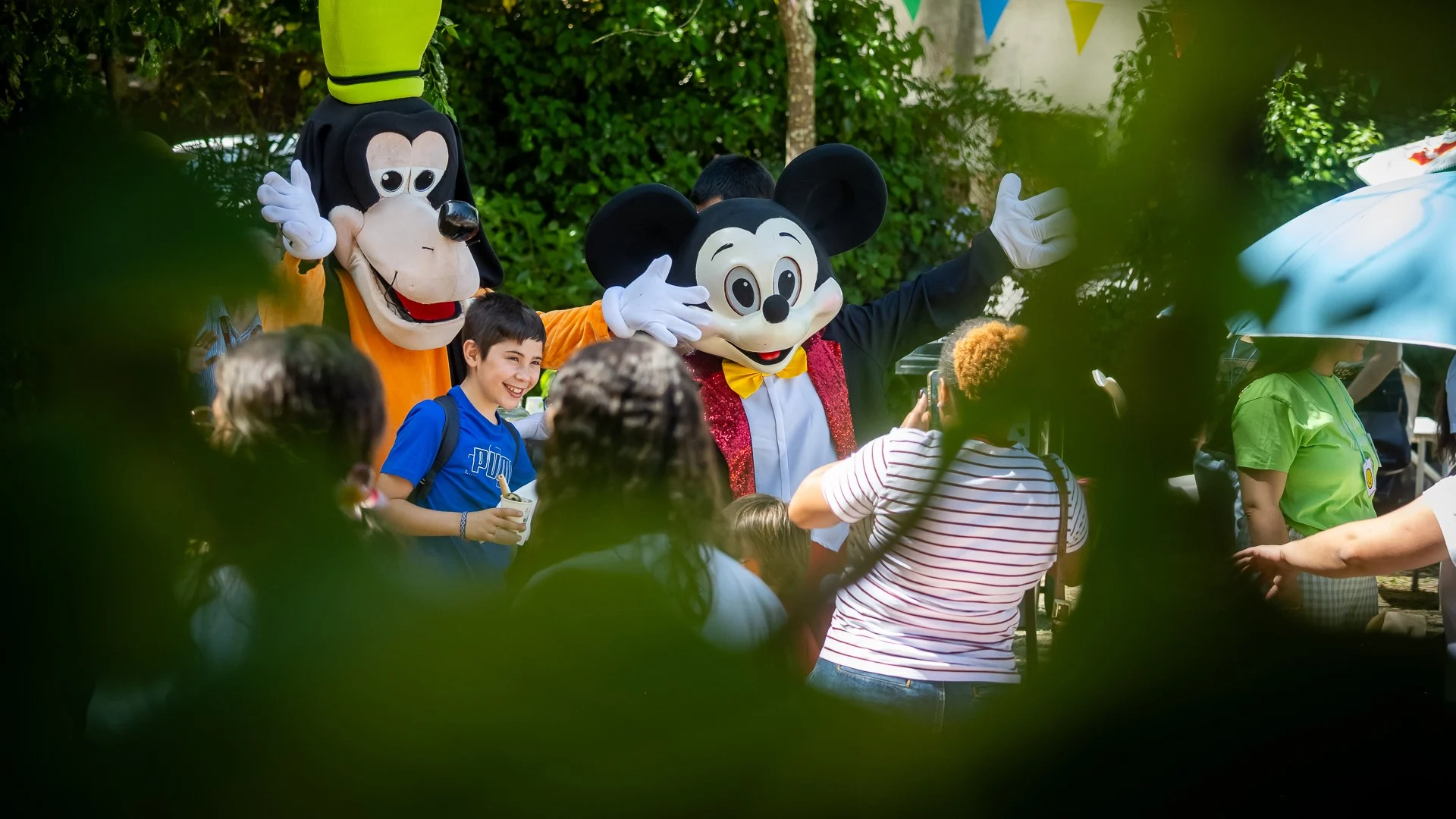 Figuras do pateta e do rato mickey posam com participantes nos jogos adaptados