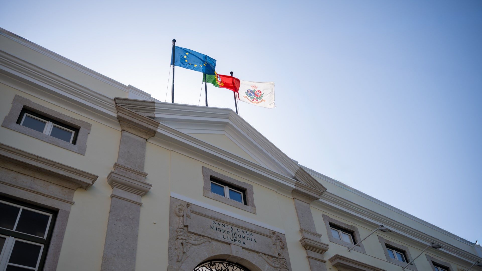 fachada de entrada da santa casa da misericordia de lisboa com bandeiras da intituição, portugal e comunidade europeia